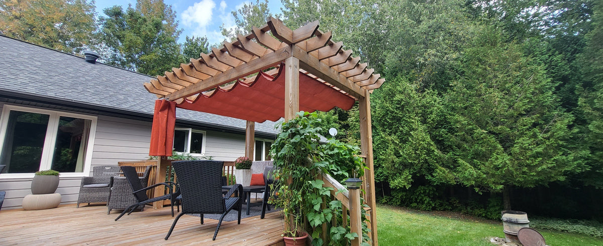 Wooden pergola with red shade fabric and climbing plants on a backyard deck — one of many creative shade sail ideas to transform small gardens into cozy retreats.