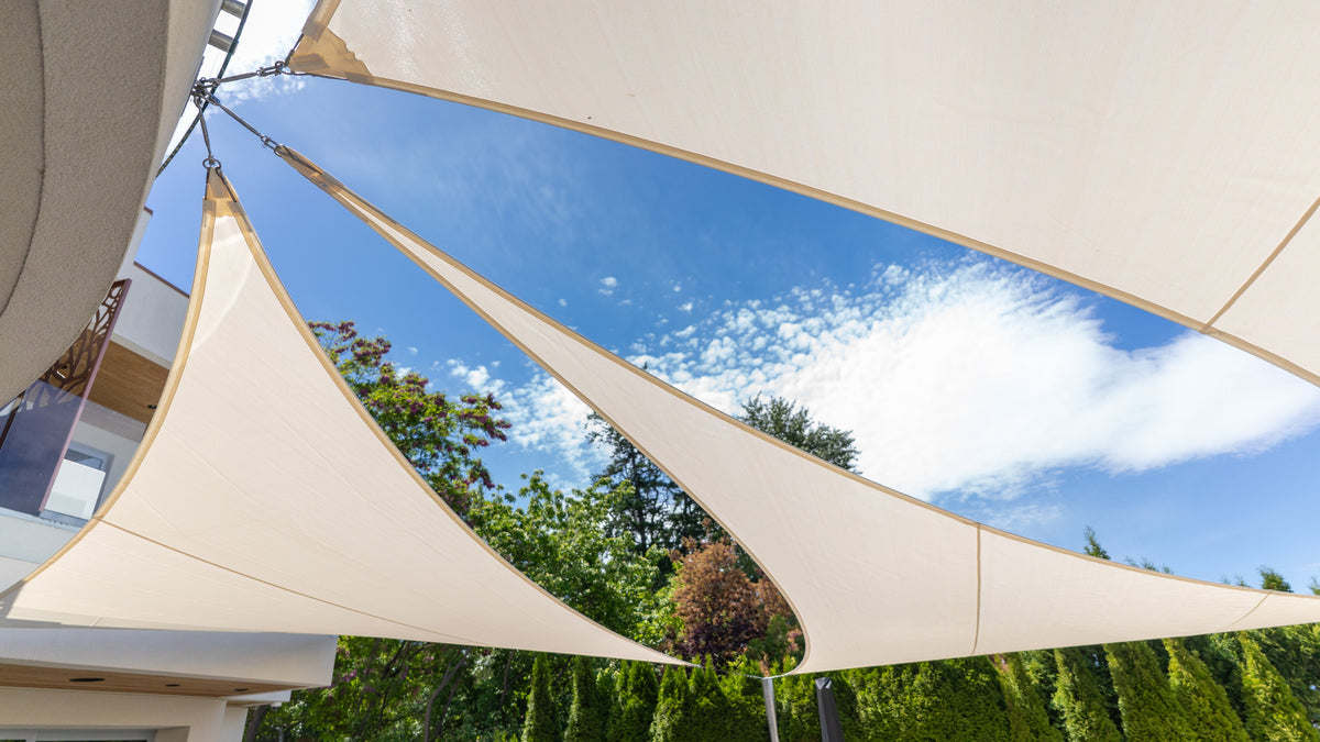 Outdoor personalized shade canopy installation featuring overlapping beige sail panels creating stylish sun protection against a bright blue sky.