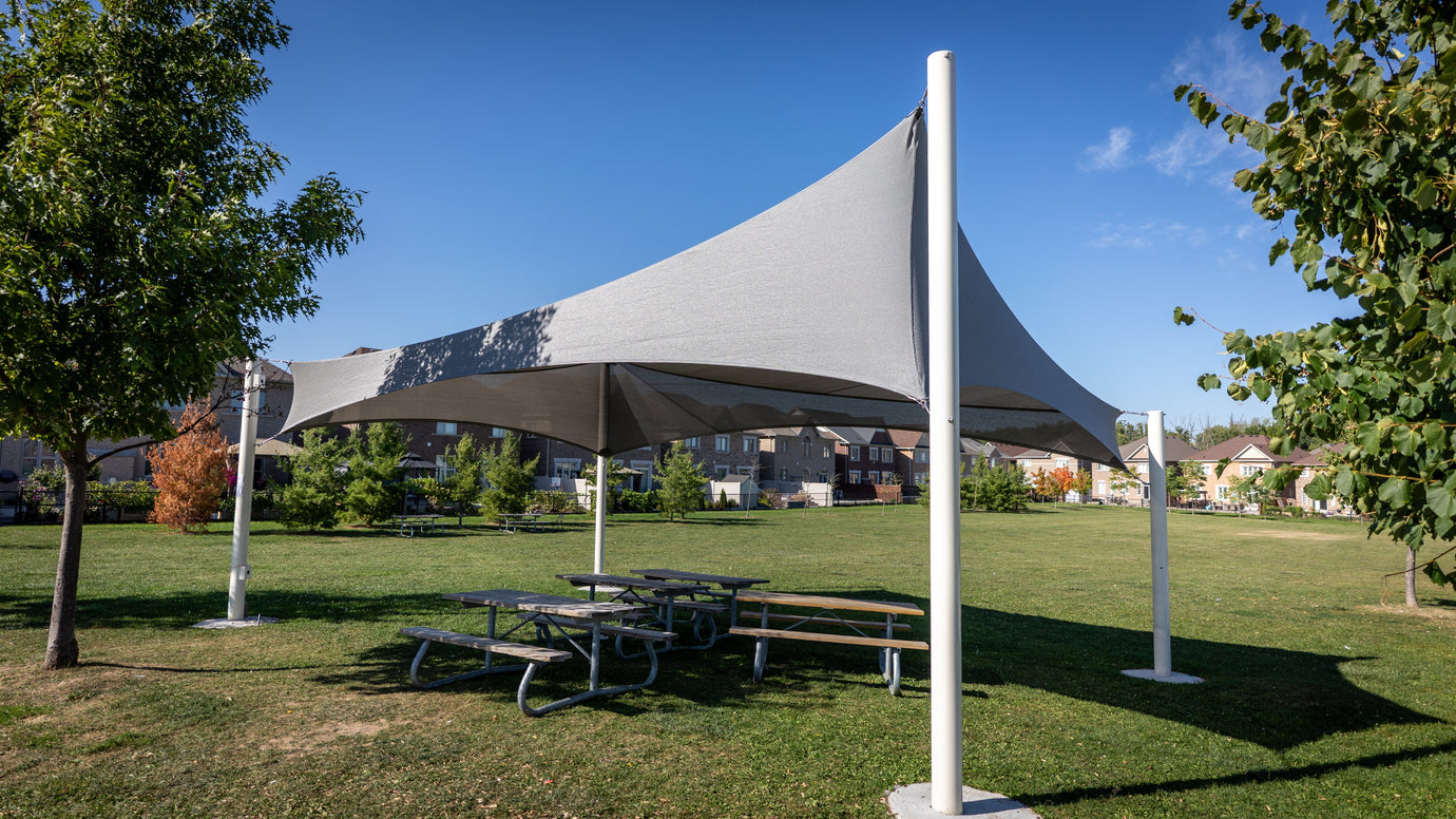 A large outdoor canopy providing shade over picnic tables in a park, showcasing durable Sun Shade Materials used for community spaces.