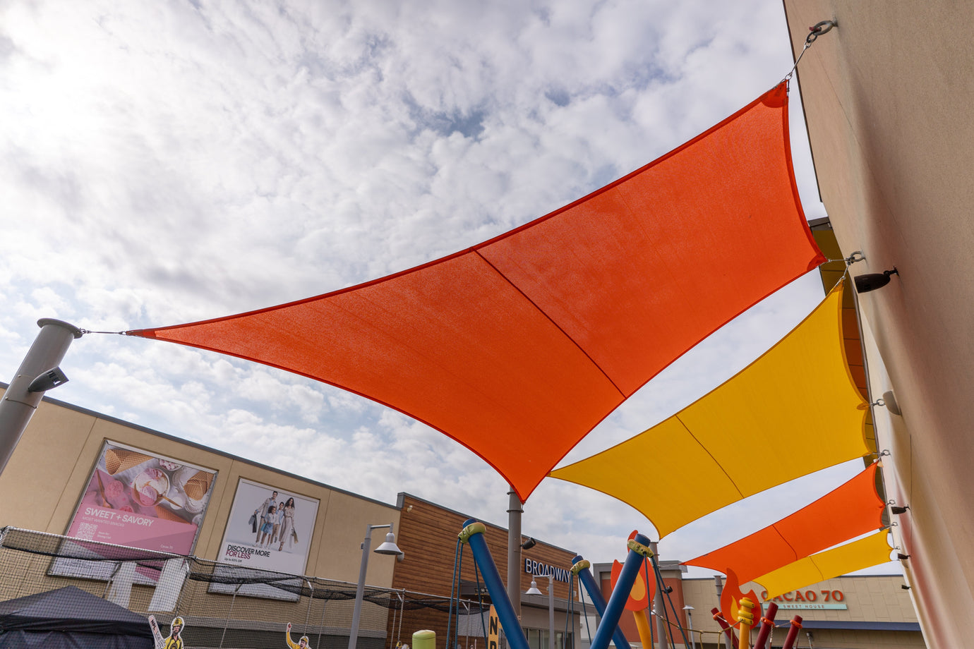 Bright orange and yellow tensile canopies installed above a playground, showcasing vibrant Shade Design for commercial outdoor spaces.