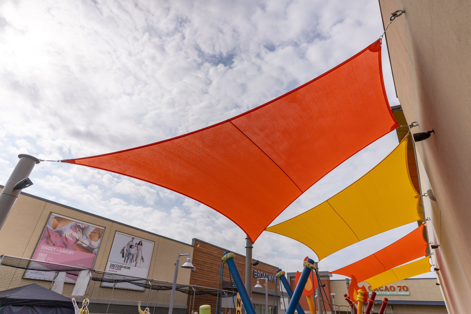 Bright orange and yellow tensile canopies installed above a playground, showcasing vibrant Shade Design for commercial outdoor spaces.