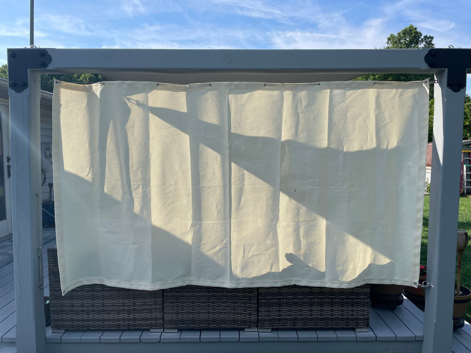 Outdoor installation of a light-colored gazebo curtain on a pergola-style frame, showcasing how to add privacy and style to your outdoor space with gazebo curtains.
