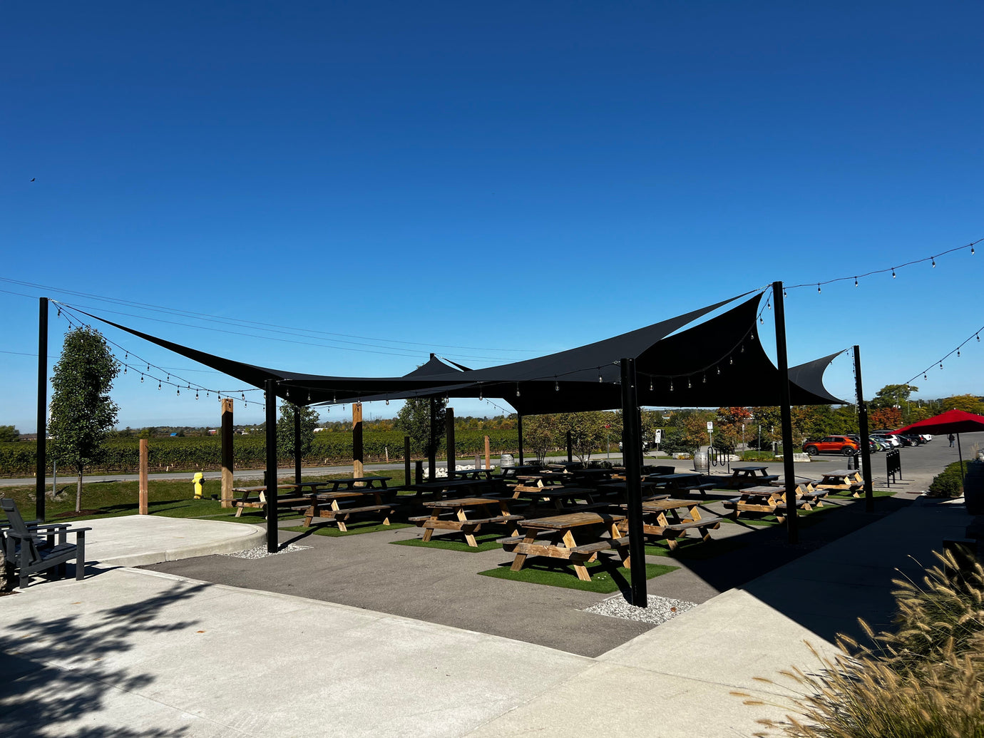 Modern black shade sails covering an outdoor picnic and dining space, showcasing energy efficiency in a commercial venue by providing broad, cool shade.
