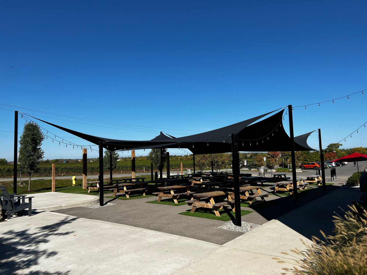 Modern black shade sails covering an outdoor picnic and dining space, showcasing energy efficiency in a commercial venue by providing broad, cool shade.