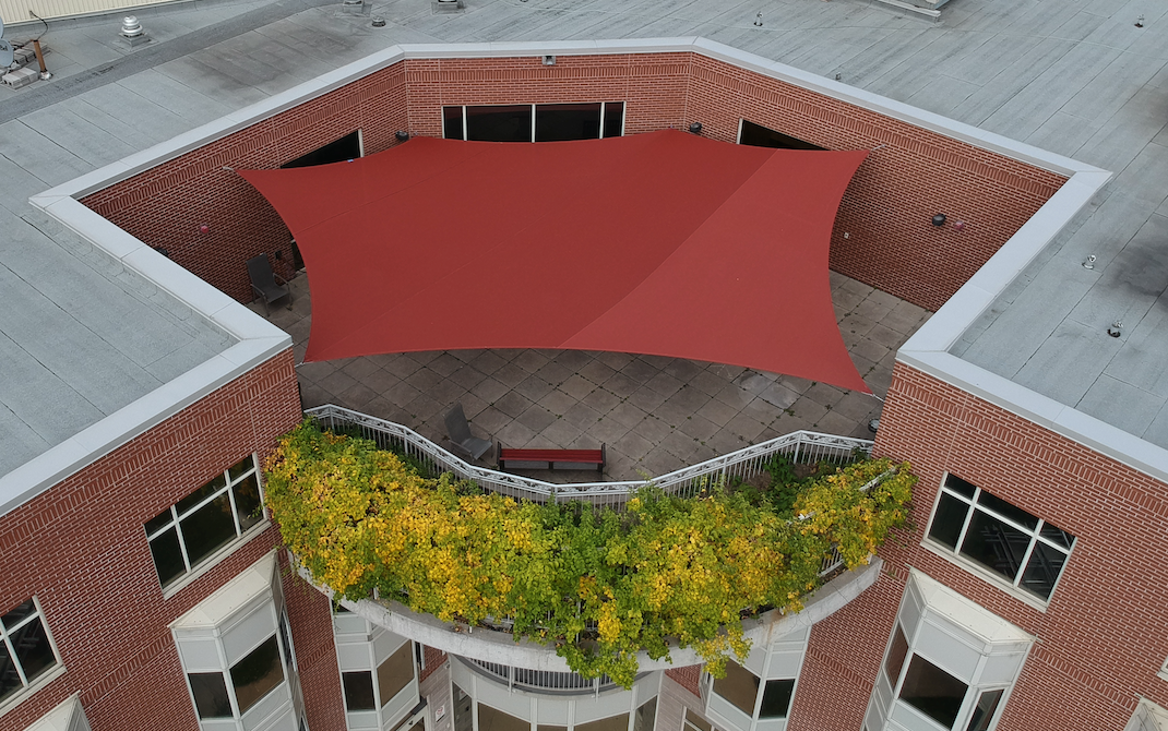 Aerial view of a custom red shade sail installed on the rooftop patio of Valleyview Retirement Residence in Toronto, providing safe and stylish outdoor coverage for residents.