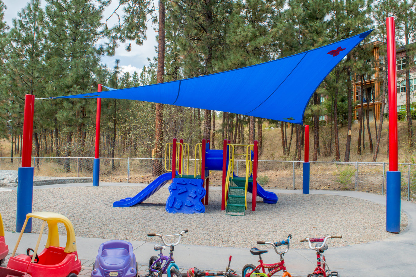 Bright blue shade sail covering a children's playground with slides and climbing equipment, providing sun protection and enhancing the outdoor play area with shade sails.